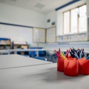 A closeup of an empty classroom with a pot of coloured pencils in red pots.