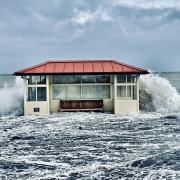 The sea crashes over one of the beach shelters in Llandudno
