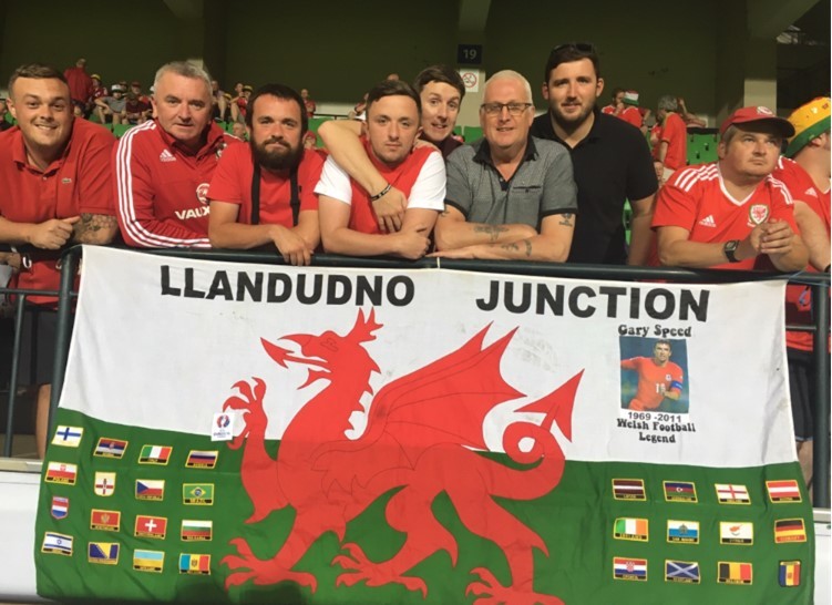 Mr Evans (centre) and fans with the famous Llandudno Junction flag, which features the flags of other countries and a tribute to former Wales manager Gary Speed.