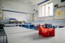 A closeup of an empty classroom with a pot of coloured pencils in red pots.