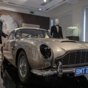 Adrian Hume-Sayer, Christie’s, Director, Head of Sale for Christie’s presses the button on the key fob to activate the machine guns out of the headlights, of the silver birch Aston Martin DB5 stunt car, one of eight stunt replicas built for