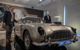 Adrian Hume-Sayer, Christie’s, Director, Head of Sale for Christie’s presses the button on the key fob to activate the machine guns out of the headlights, of the silver birch Aston Martin DB5 stunt car, one of eight stunt replicas built for